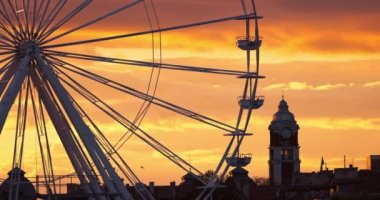 Dönme dolap lunaparkta ve manzaralı günbatımı bulutları gökyüzünde ve uçan kuşlar binaların etrafında.