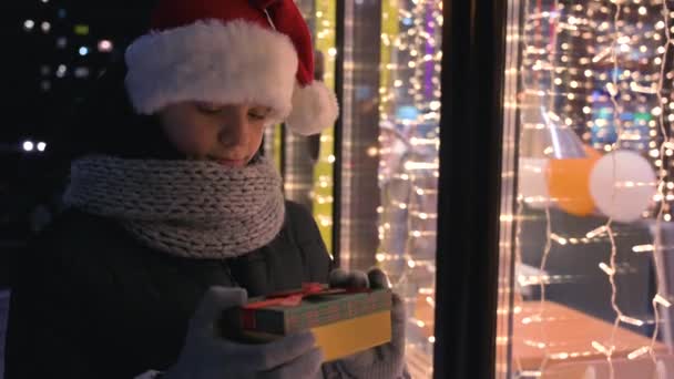 Menino em chapéu Santas com caixa de presentes olhando e sonhando — Vídeo de Stock