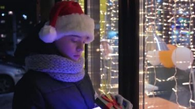 Noel Baba şapkalı çocuk hediye kutusuyla bakıyor ve hayal kuruyor.