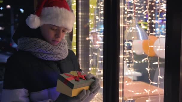 Menino em chapéu Santas com caixa de presentes olhando e sonhando — Vídeo de Stock