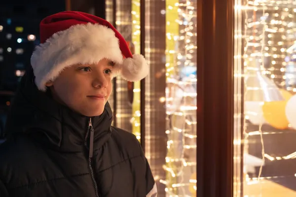 Boy in Santas hat looking in shop window — Stock Photo, Image