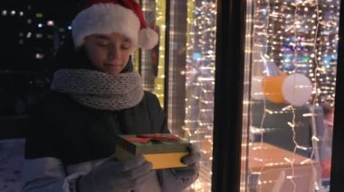 Noel Baba şapkalı çocuk hediye kutusuyla bakıyor ve hayal kuruyor.