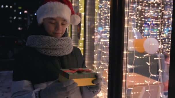 Niño en sombrero de Santas con caja de regalos mirando y soñando — Vídeo de stock