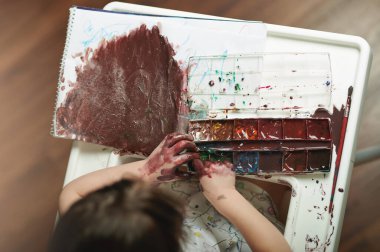 Çocuk dağınık ve masa üstünde boya var.