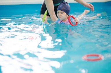 Çocuk teması için yüzme egzersizi. Çocuk havuzda yüzmeyi öğreniyor.