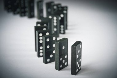 Beyaz arka planda siyah domino taşları zinciri. Domino etkisi kavramı