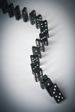 Beyaz arka planda siyah domino taşları zinciri. Domino etkisi kavramı