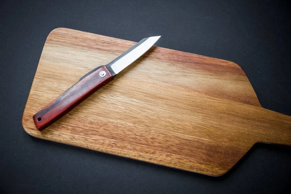 Traditional japanese higonokami pocket knife on a wooden cutting board. Black background