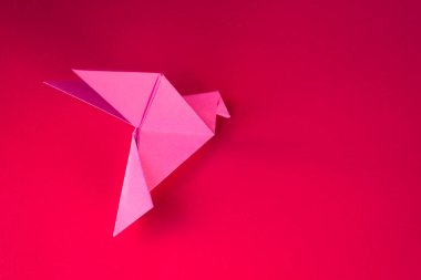 Pembe kağıt güvercin origamisi boş kırmızı bir arkaplanda izole edilmiş..