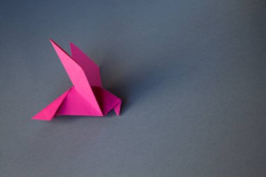 Pembe kağıt güvercin origamisi gri bir arkaplanda izole edilmiş..