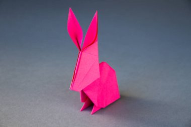 Pembe kağıttan tavşan origamisi boş gri bir arkaplanda izole edilmiş..