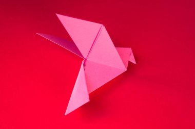 Pembe kağıt güvercin origamisi boş kırmızı bir arkaplanda izole edilmiş..