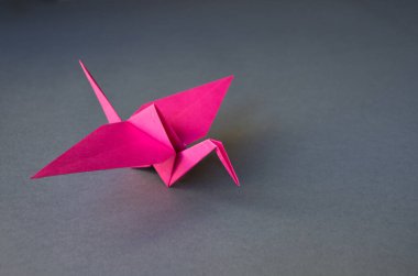 Pembe kağıt turna origamisi boş gri bir arkaplanda izole edilmiş..