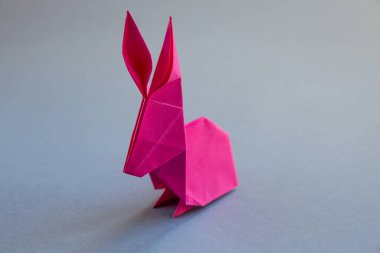 Pembe kağıttan tavşan origamisi boş gri bir arkaplanda izole edilmiş..