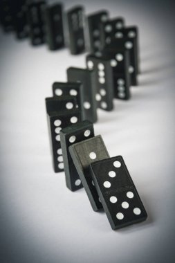Beyaz arka planda siyah domino taşları zinciri. Domino etkisi kavramı