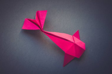 Pembe kağıttan balık origamisi boş gri bir arkaplanda izole edilmiş.