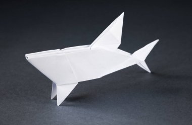 Beyaz kağıt köpek balığı origamisi gri bir arkaplanda izole edilmiş.
