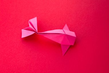 Pink paper fish origami isolated on a blank red background