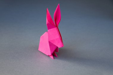 Pembe kağıttan tavşan origamisi boş gri bir arkaplanda izole edilmiş..