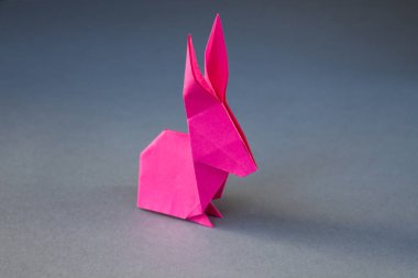 Pembe kağıttan tavşan origamisi boş gri bir arkaplanda izole edilmiş..