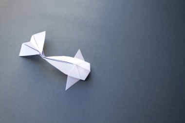 Beyaz kağıt balığının origamisi gri bir arkaplanda izole edilmiş.