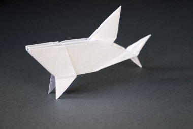 Beyaz kağıt köpek balığı origamisi gri bir arkaplanda izole edilmiş.