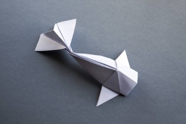 Beyaz kağıt balığının origamisi gri bir arkaplanda izole edilmiş.