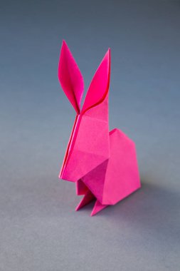 Pembe kağıttan tavşan origamisi boş gri bir arkaplanda izole edilmiş..