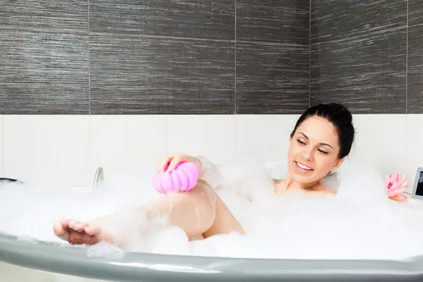 Bella donna sorriso lavaggio gamba con spugna rosa in bagno con schiuma — Foto Stock