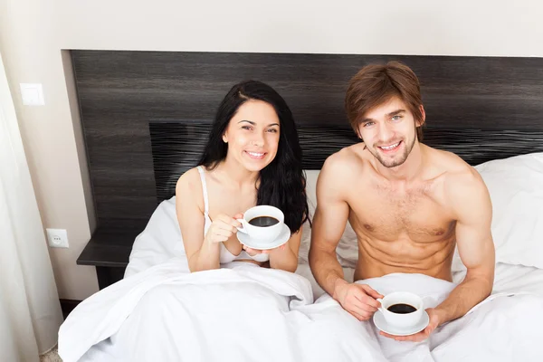 若いカップルはベッドの中でコーヒーを飲む — ストック写真