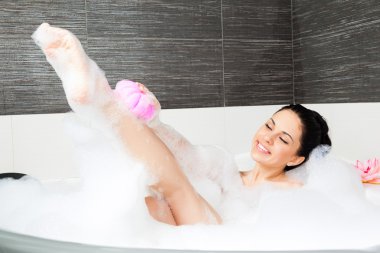 Woman washing leg with pink sponge