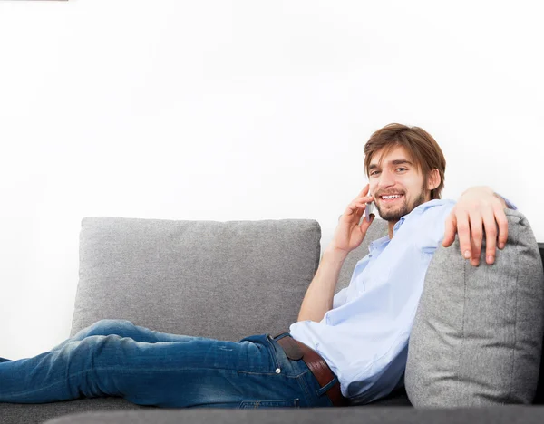 Hombre joven tumbado relajado en el sofá hablando por teléfono — Foto de Stock