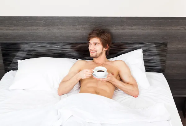 Hombre guapo acostado en la cama por la mañana con café —  Fotos de Stock