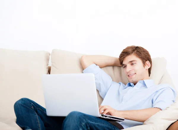 リラックスできるコンピューターとソファの上に横たわって若い人 — ストック写真
