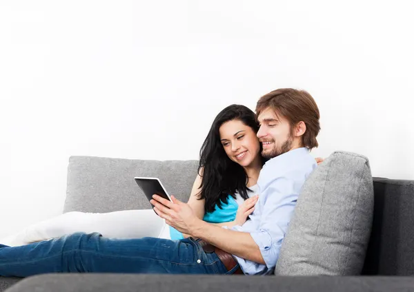 Casal jovem sentado em um sofá usando tablet — Fotografia de Stock