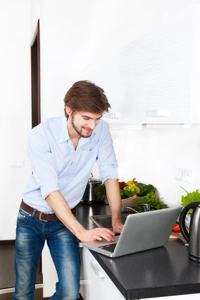 Jonge man op keuken thuis gelukkig glimlach met behulp van laptop koken — Stockfoto