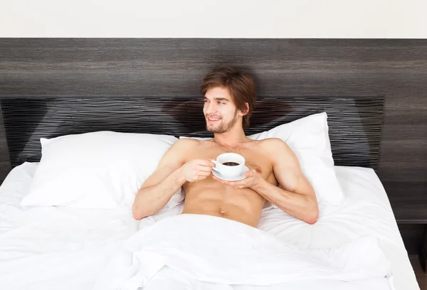 Beau homme allongé sur le lit boire du café — Photo