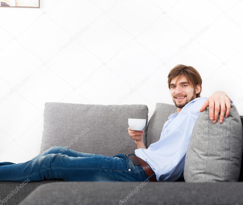 Young man lying relaxing on the couch with cup of tea