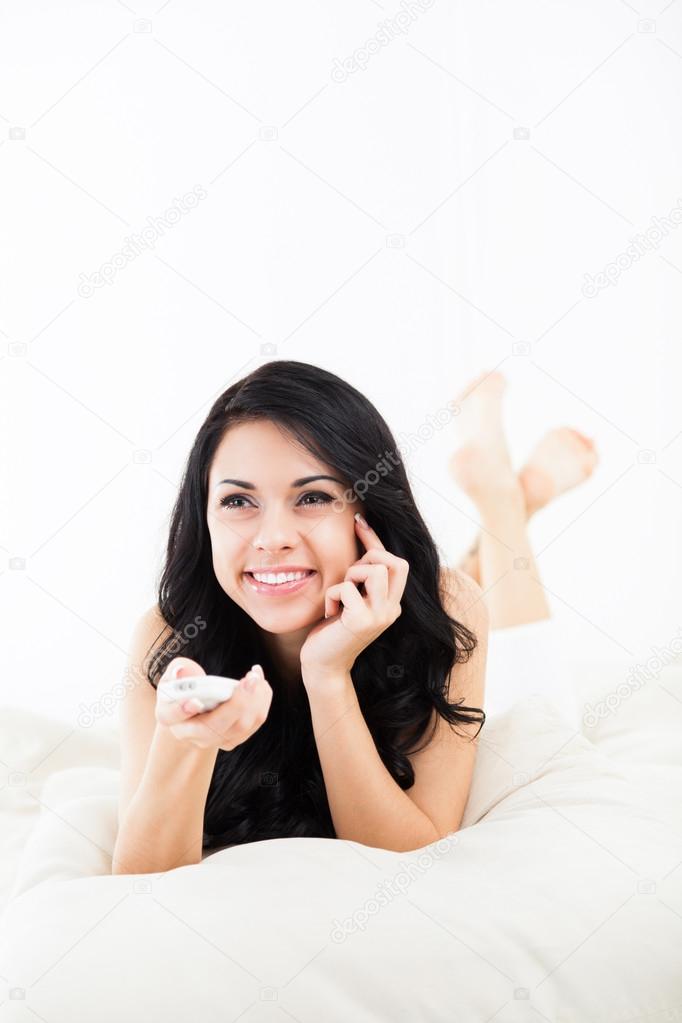 Woman smile watching tv hold remote control, young happy girl lying on couch