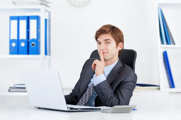 Бизнесмен с пальцем на губах сидит в офисе — стоковое фото