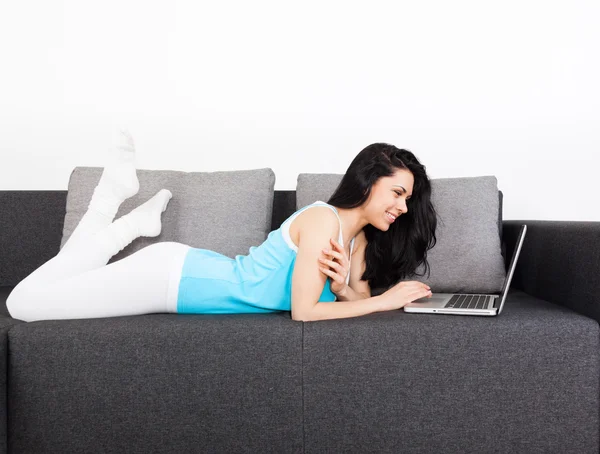 Женщина с ноутбуком лежит на диване дома — стоковое фото