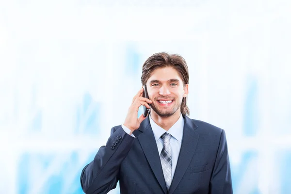 Businessman talking on mobile phone in bright blue office — Stock Photo, Image