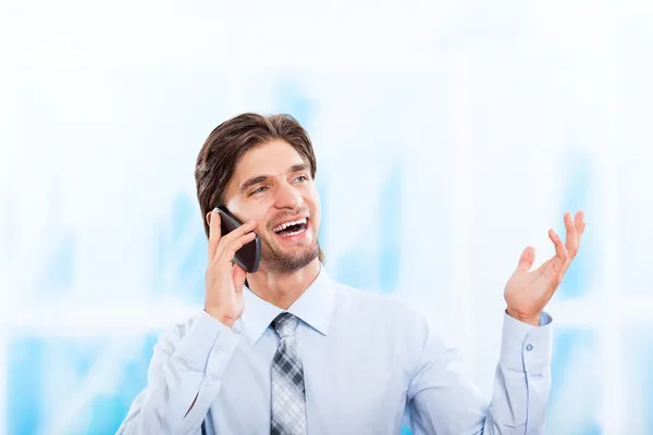 Businessman talking on mobile phone in bright blue office — Stock Photo, Image