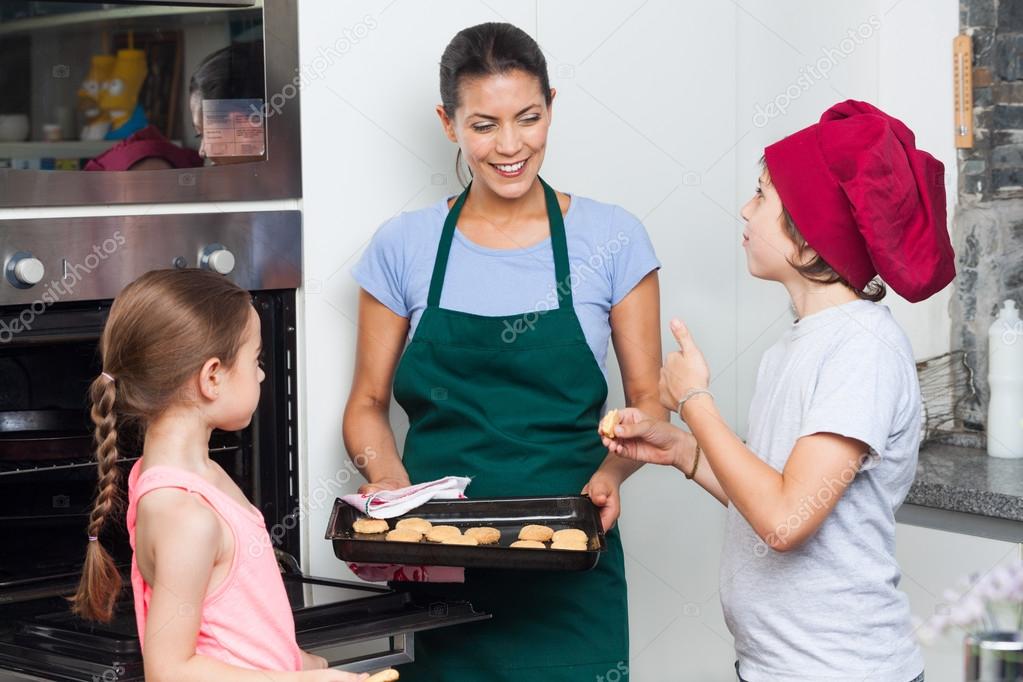 Mother and children taking cookies from oven