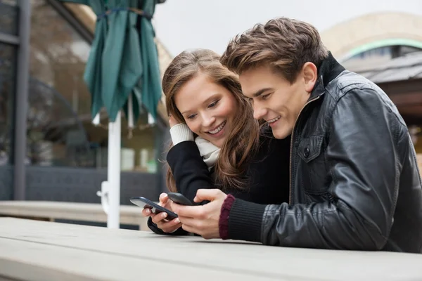Paar benutzt Handy, während es sich auf Bank lehnt — Stockfoto