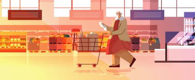 Alışveriş arabasıyla dolu son sınıf öğrencisi kadın süpermarket modern bakkal dükkanında alışveriş listesini kontrol ediyor.