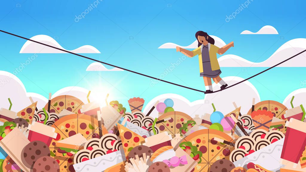 schoolgirl balancing on rope above junk food assortment of fast food unhealthy nutrition junkfood addiction concept