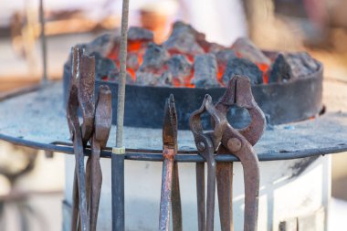 blacksmith hand holding tongs with metal piece and heating it in fire before forging . Blacksmithing concept.