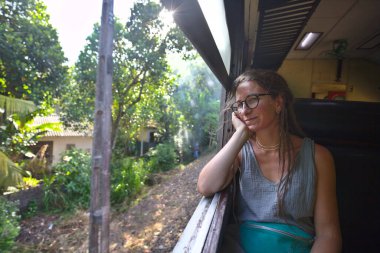 Sri Lanka 'nın dağlık bölgelerindeki çay tarlaları arasında Ella' dan Kandy 'ye tren yolculuğunun tadını çıkaran genç bir kadın.