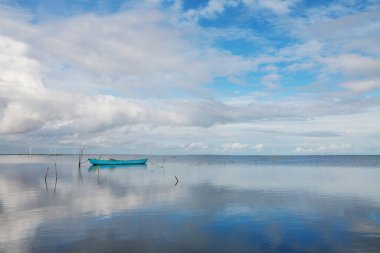 Mavi bir gölde yansıyan bulutları olan mavi bir tekne. Sri Lanka, Asya.